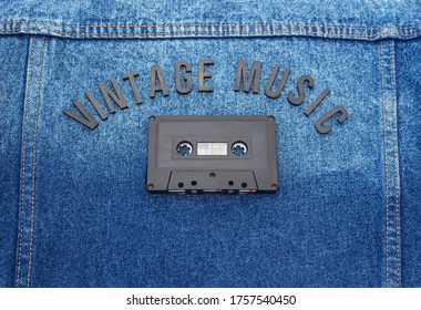 Top View Of A VINTAGE MUSIC Black Lettering Word With An Old Black Cassette Over A Jean Jacket. Fashion And Music Concept