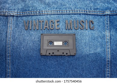 Top View Of A VINTAGE MUSIC Black Lettering Word With An Old Black Cassette Over A Jean Jacket. Fashion And Music Concept