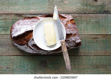 Top view of a wake bread, a plate with butter and a knife on a rustic wooden table. 