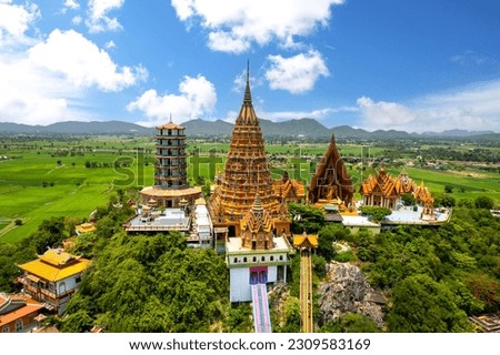 Top view of  Wat Tham Sua, chinese shrine temple on top hill with green rice fields and blue sky in Kanchanaburi Thailand