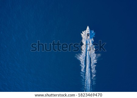 Top view of a white boat sailing to the blue sea. Large speed boat moving at high speed. Travel - image. Drone view of a boat sailing. Motor boat in the sea.