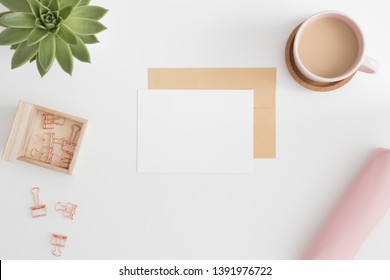 Top View Of A White Card Mockup And Envelope With Workspace Accessories On A White Table.