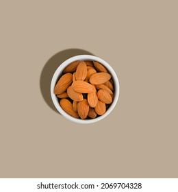 Top view of a white ceramic bowl with almonds on a beige background. Hard shadow and light. Monochrome image.