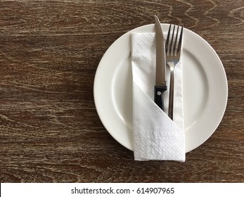 Top view of white circle plate, knife and fork on wooden table