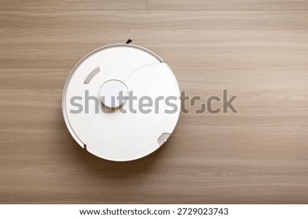 Top View of a White Circular Robotic Vacuum Cleaner on a Wooden Floor