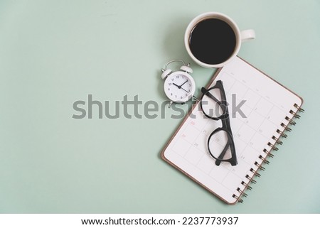 top view of white clock with  glasses on planner, and blurred hot coffee cup on a light green background including copy space. For planning business, working space concept