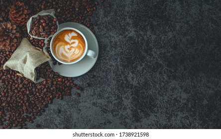 Top view, White coffee cup of hot latte art coffee and coffee bean placed on dark stone background. Menu in coffeeshop, relaxing time holidays.