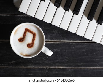 Top View White Cup Of Coffee With Musical Note Symbol On Frothy Surface Flat Lay On Black Painted Wood Table With Keyboard. Enjoy Coffee And Music, Food Art Creative Concept / Close Up, Space For Text