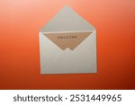 Top view of white envelope and postcard with brown card with words "Welcome" written on it. Welcome greeting for invitation, express hospitality, greet, show acceptance.