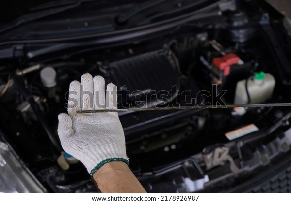 Top view of a white gloved man holding a dipstick\
to check the oil level. close up of mechanic’s hand wearing white\
gloves holding a dipstick to check the oil level for engine\
maintenance and repair.