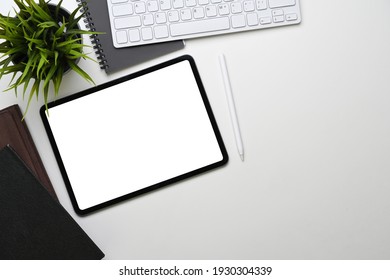 Top View Of White Office Desk With Digital Tablet, Keyboard, Notebook And Plant.