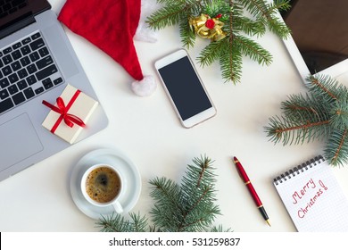 Top View Of White Office Table With Cropped Laptop Electronic Gadgets And Christmas Theme Items