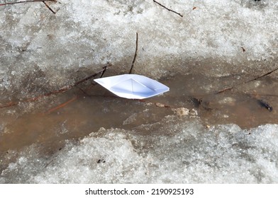 Top View Of White Paper Boat Sails Along A Spring Stream Among The Snowy Shores