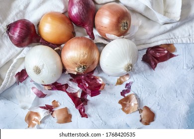 A top view of white and purple onions and onion peelings on a white kitchen towel