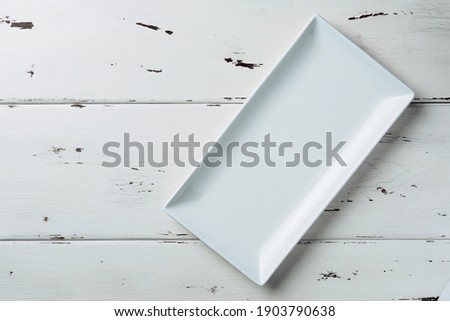 Top view of a white rectangular plate on a white wooden background. Flat lay. Copy space.