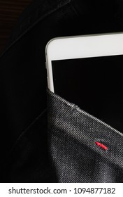 Top view of white smartphone into the pocket in black jeans. Vertical