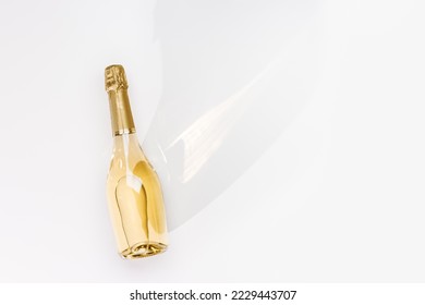 Top view white sparkling wine bottle with sunshine long shadow and flare on light white background. Minimal aesthetic flat lay, one champagne bottle with golden foil. Summer alcohol drinks, copyspace