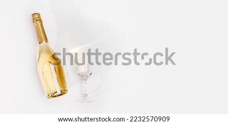 Top view white sparkling wine bottle and glass wine with sun shadow and glare on light white background. Flat lay  golden champagne bottle. Summer alcoholic drink concept, banner with copyspace, above