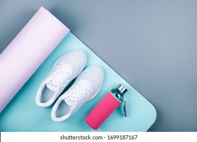 Top view of white sport shoes (sneakers) blue pink yoga mat,glass water bottle  on pastel grey background. Yoga pilates or fitness practice. Losing weight and sport concept. Flat Lay. 