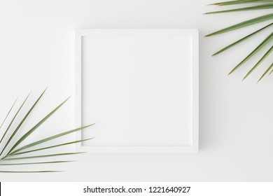 Top view of a white square frame mockup with palm leaf decoration.