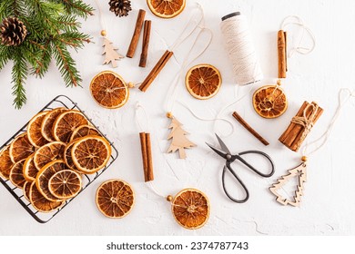 Top view of white textured background with homemade garland of dried oranges, spruce branches, orange slices and craft scissors. Flat lay. decoration - Powered by Shutterstock