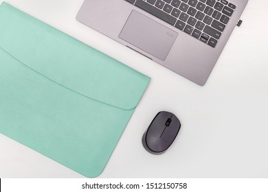 Top View Of White Working Table With Modern Laptop, Mint Color Leather Case For Personal Computer And Wireless Mouse. Work Space For School Or Office. Copy Space. Flat Lay.