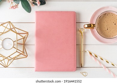 Top view of white working table background with blank paper notebook, cup of coffee. Flat lay green leaf, flowers, golden paper binder clips. Notepad and pen. Desktop mockup, workspace, stationery.