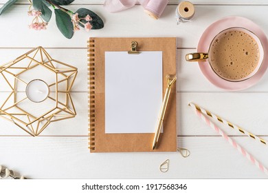 Top View Of White Working Table Background With Blank Paper Notebook, Cup Of Coffee. Flat Lay Green Leaf, Flowers, Golden Paper Binder Clips. Notepad And Pen. Desktop Mockup, Workspace, Stationery.