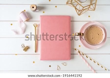 Top view of white working table background with blank paper notebook, cup of coffee. Flat lay green leaf, flowers, golden paper binder clips. Notepad and pen. Desktop mockup, workspace, stationery.