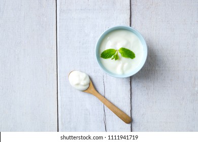 Top View Of White Yogurt On Blue Sky Cup And Wooden Spoon On White Wood.