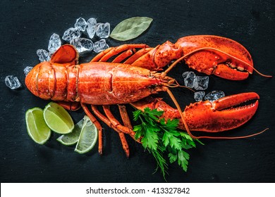 Top view of whole red lobster with ice and lime on a black slate plate