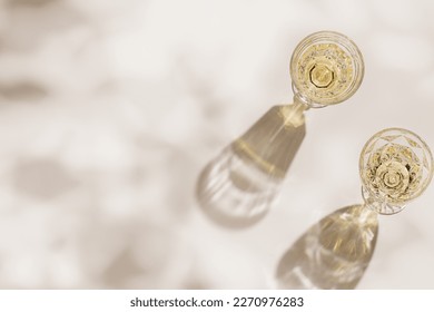 Top view of wineglasses with white wine, leaves shadow and glare from glass at sunlight, summer alcohol drink background beige monochrome, creative aesthetic view of wine glass goblets style on table - Powered by Shutterstock