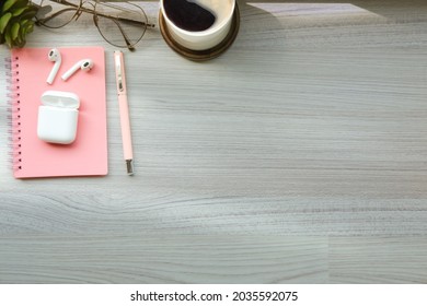 Top view wireless earphone, notebook, glasses and coffee cup on wooden table.