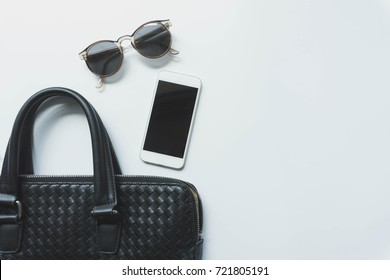 Top View Of Woman Black Bag Open Out With Accessories Smartphone And Sunglasses On White Background.