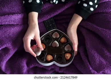 Top View Of Woman With Blanket Eating Heart Chocolates From Heart-shaped Gift Box