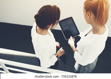 Top view of woman CEO is holding touch pad with mock up copy space on the screen, while is standing with client in corridor company. Two female are watching video on digital tablet before conference - Powered by Shutterstock