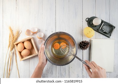 Top view of woman chef breaking an egg into the  bowl. Female chef whisking eggs in bowl on white table - Powered by Shutterstock