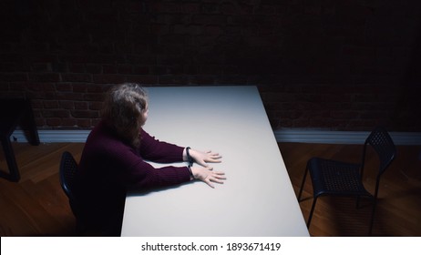 Top view of woman criminal with handcuffs sitting in interrogation room. Female suspect handcuffed sitting at table waiting for police officer in department