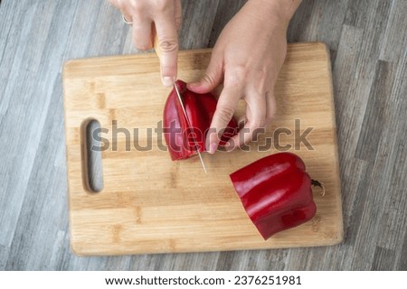 Top view of woman cutting bell pepper in kitchen, closeup. Woman hands cut bell pepper on wooden board. Close up view of female hands cutting bell pepper for salad on wooden cutting board