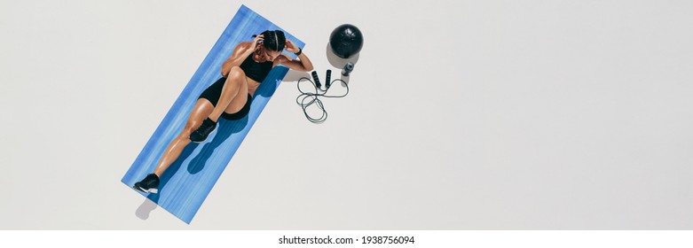 Top View Of A Woman Doing Abdomen Exercises On A Fitness Man. Woman In Sportswear Doing Abs Crunches With A Medicine Ball And Skipping Rope By Her Side On Floor, With Lots Of Copy Space.