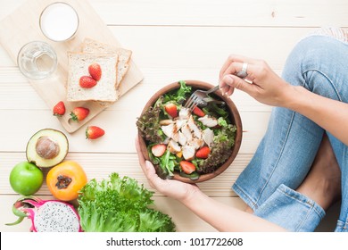 Top view woman eating chicken salad with fruits, vegetables, whole wheat bread and milk on wooden background, Healthy food