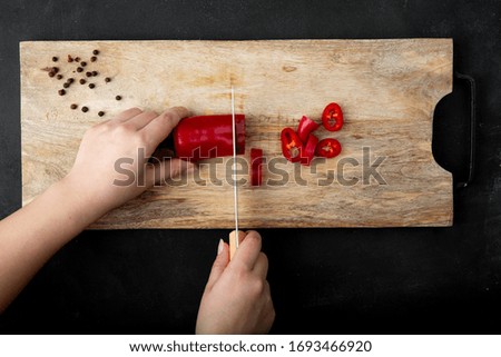 top view of woman hand cutting pepper on cutting board with pepper spice on black background