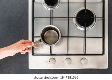 Top View Of Woman Hand Holding Pan On Modern Kitchen Gas Stove Cooker With Burner. Housewife Cooking Food, Boiled Water And Using Metal Kitchenware