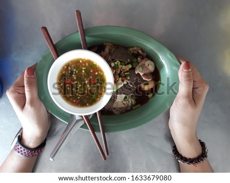 Top view, woman hand holding a cup of braised beef noodles in an Asian restaurant