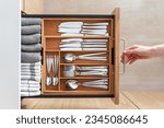 Top view of woman hand opening drawer with wooden cutlery tray. Separated section for knives, spoons, forks and linen towels. Storage of shiny silverware in the kitchen