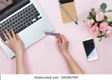 Top View Of Woman Hands Holding Credit Card, Online Shopping Concept, Workspace With Laptop, Mobile Phone, Flowers And Notebook, Flat Lay.