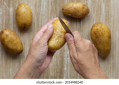 Top View Of Woman Hands Holding Boiled Potato In Jacket To Scrub With Knife On Wooden Background