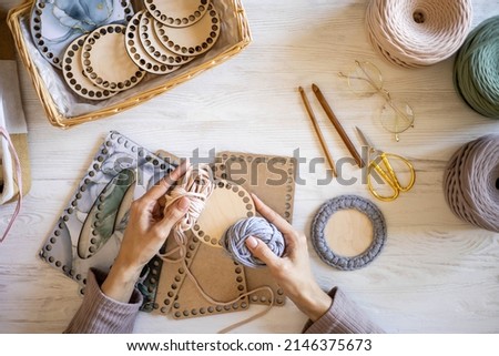 Top view woman hands knitted accessory interior decor use ribbon yarn and wooden stencil pattern on desk table at home. Closeup female arms creating exclusive handmade craft details art work