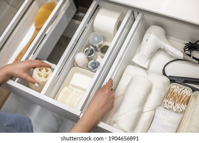 Top view of woman hands neatly organizing bathroom amenities and toiletries in drawer or cupboard in bathroom. Concept of tidying up a bathroom storage by using Marie Kondo's method.