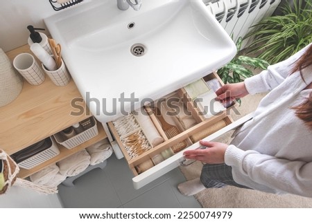 Top view of woman hands neatly organizing bathroom amenities and toiletries in drawer or cupboard in bathroom. Concept of tidying up a bathroom storage by using Japanese method.